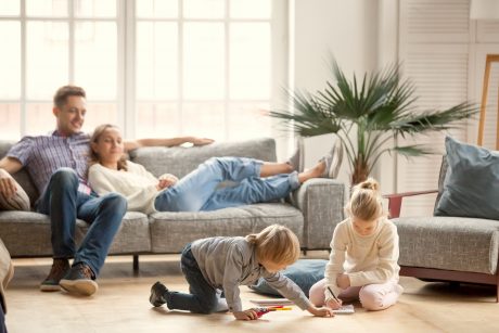 Children Sister And Brother Playing Drawing Together On Floor While Young Parents Relaxing At Home O